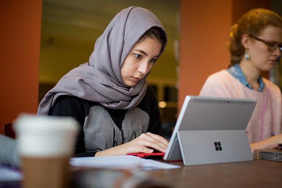 Photo of a Chatham University student in a hijab, working on a tablet in Cafe Rachel
