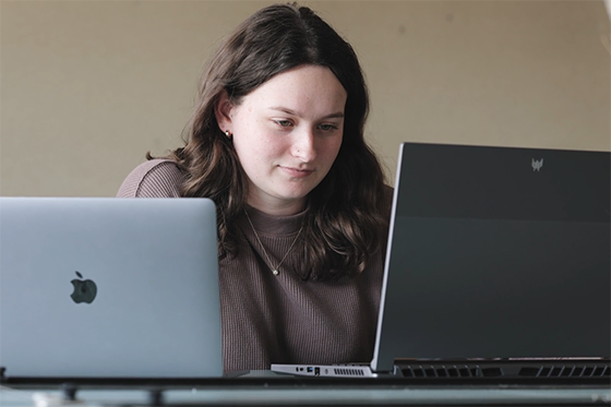 图为一名学生在两台电脑前工作，其中一台有苹果公司的标志