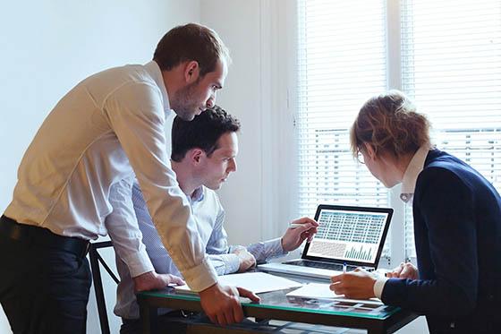Photo of a group of three business professionals surrounding a computer, working together on a project.