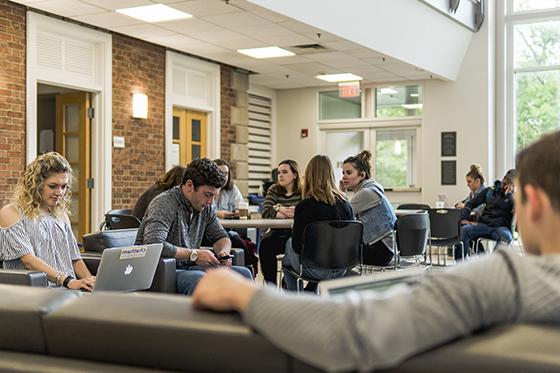 Photo of Chatham University students working on laptops on couches and at tables in an academic building.