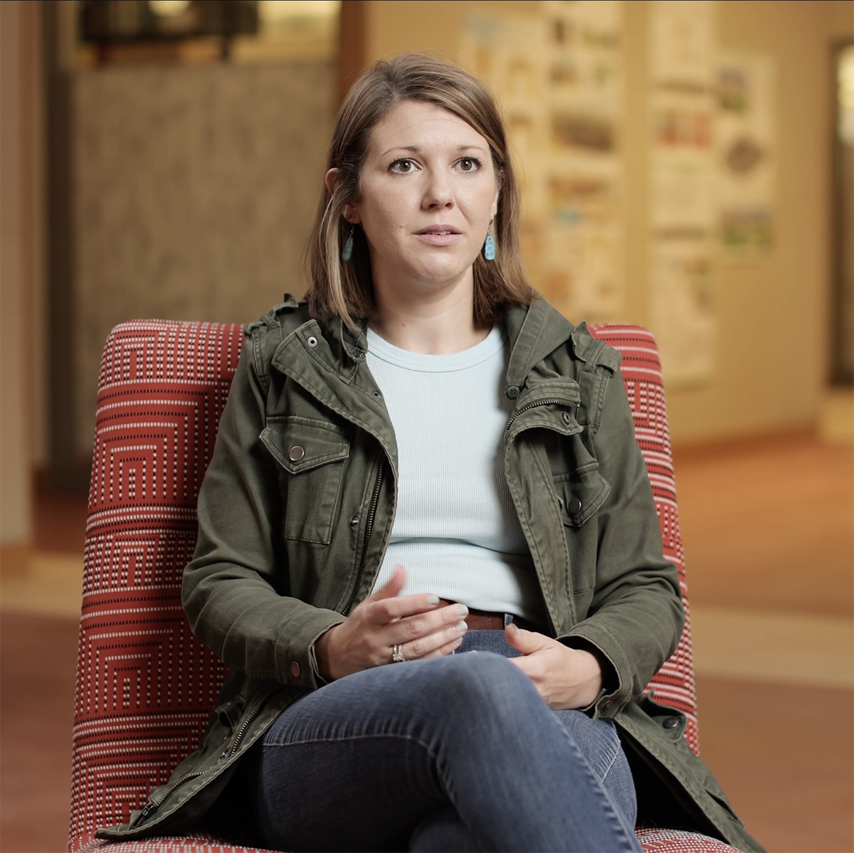 Photo of an alumna seated in a red chair, speaking to a video interviewer
