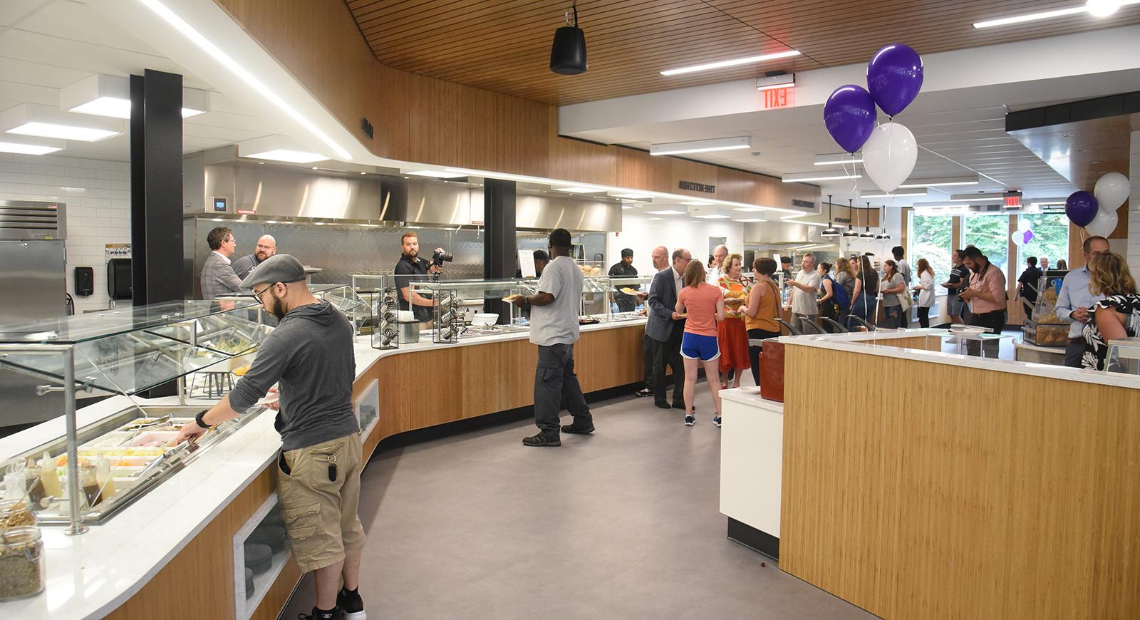 Photo of people serving food to themselves in Anderson Dining Hall on opening day, with some purple balloons nearby